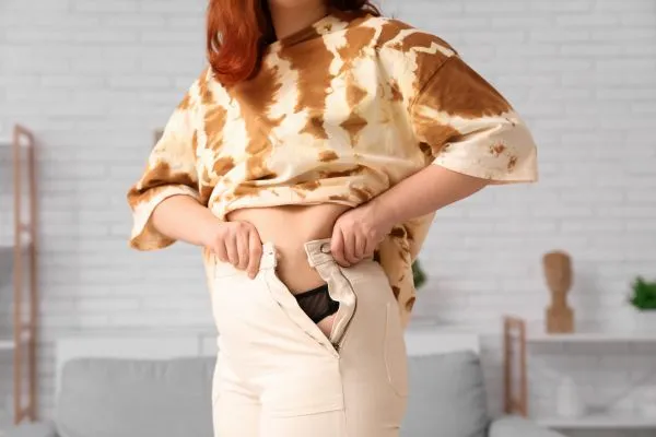 Image of woman trying to do her trousers up after pregnancy weight gain Hockley