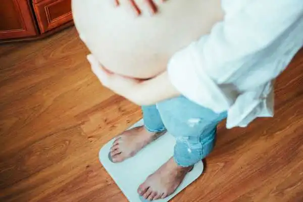 Image of woman weighing herself and experiencing weight gain through pregnancy Hockley